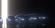 Siluetas de autos modernos con luces encendidas en penumbra.