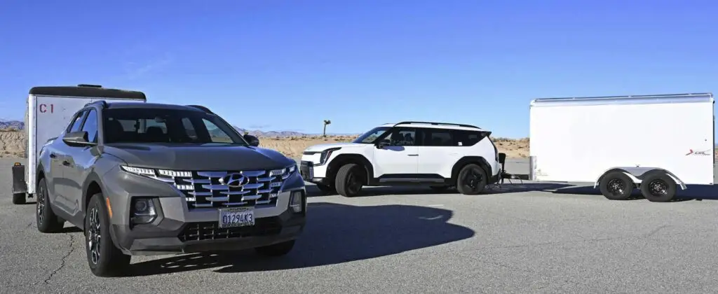 Dos vehículos estacionados junto a un remolque en un desierto.