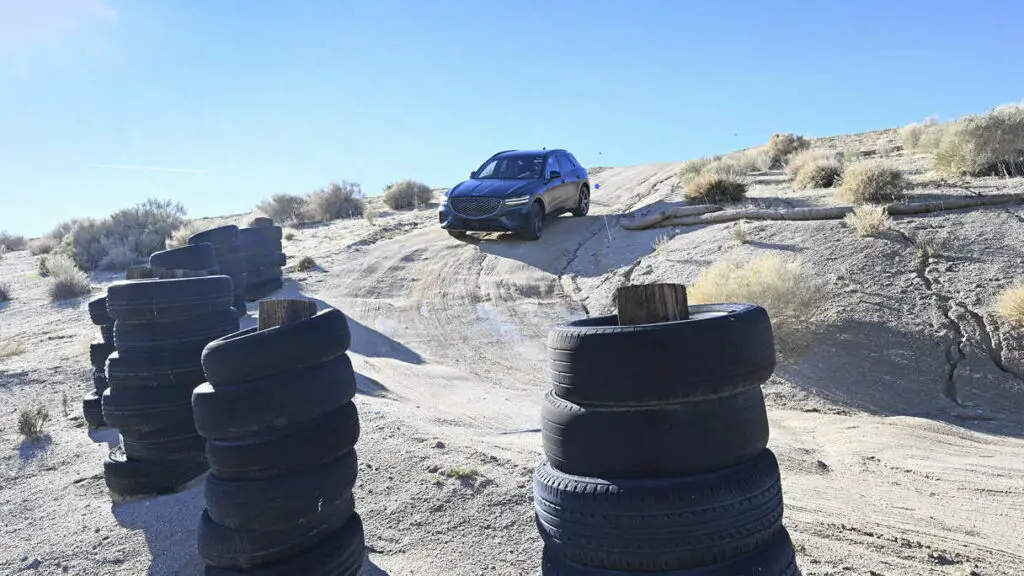 Coche en terreno arenoso entre pilas de neumáticos usados.