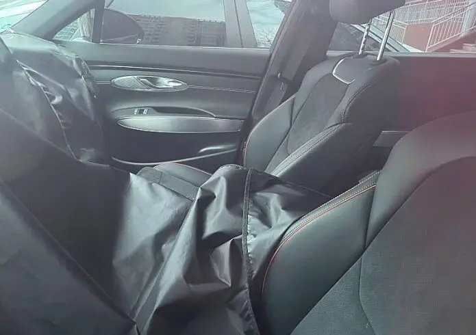 Interior de un vehículo con asientos cubiertos por una tela negra.