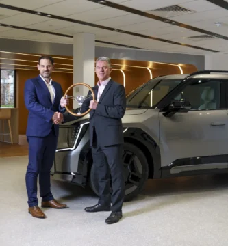 Dos hombres en trajes sostienen un trofeo junto a un coche moderno.